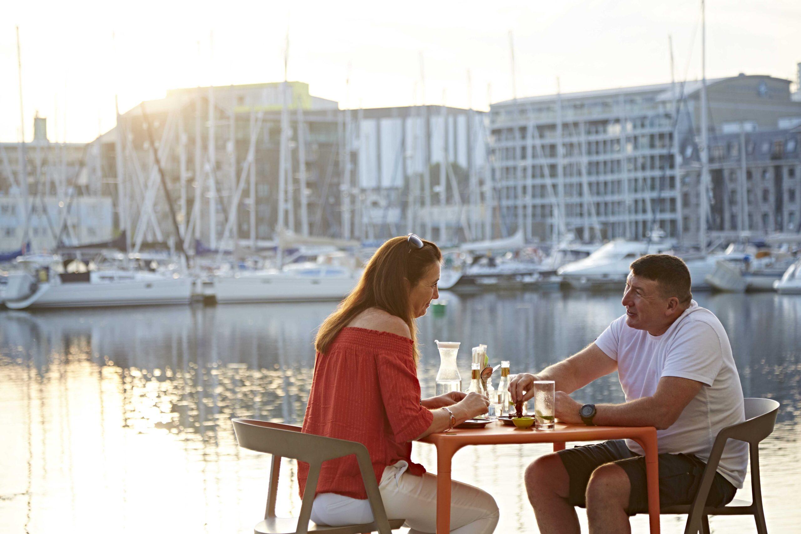 A couple dining at Supha's, next to the water as the sun sets, during their weekend getaway to Sutton Harbour.