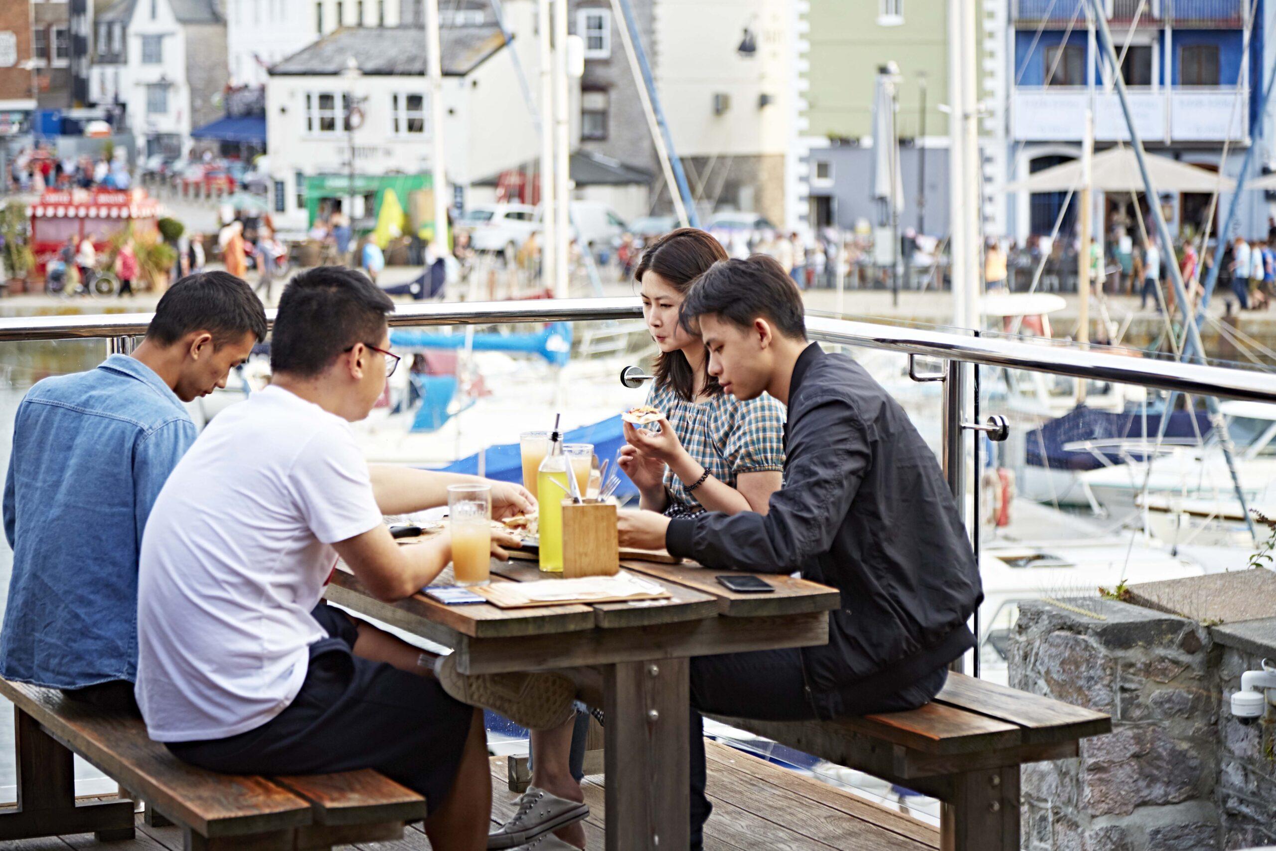 A group of students sit on Sutton Harbour enjoying food and drinks.