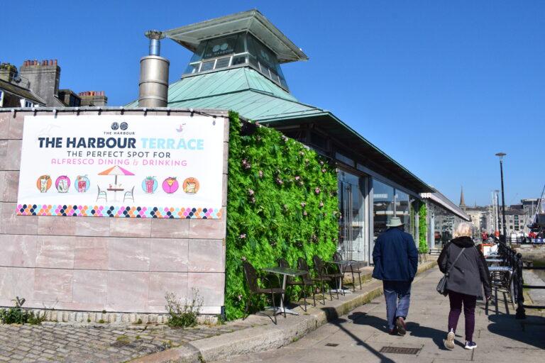 A sunny day at Sutton Harbour showing two people walking beside The Harbour fish and chip shop.