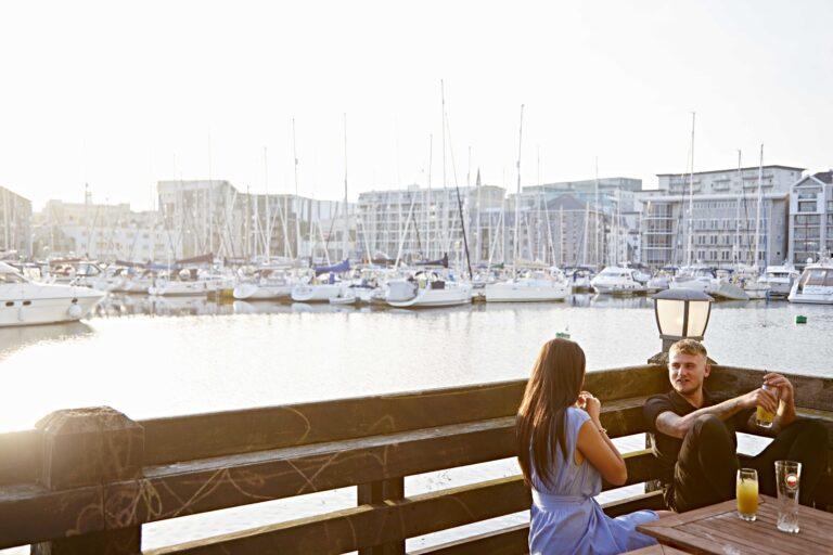 A couple on a date dine alfresco next to Sutton Harbour in the glow of the sun