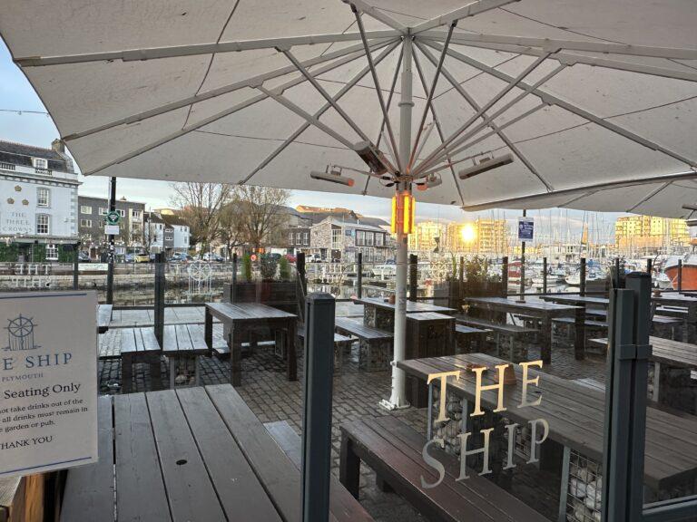 The outside seating at The Ship, we see benches with large umbrellas over the top looking out towards the harbour