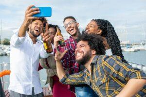 A group of people holding alcohol pose for a selfie on a boat
