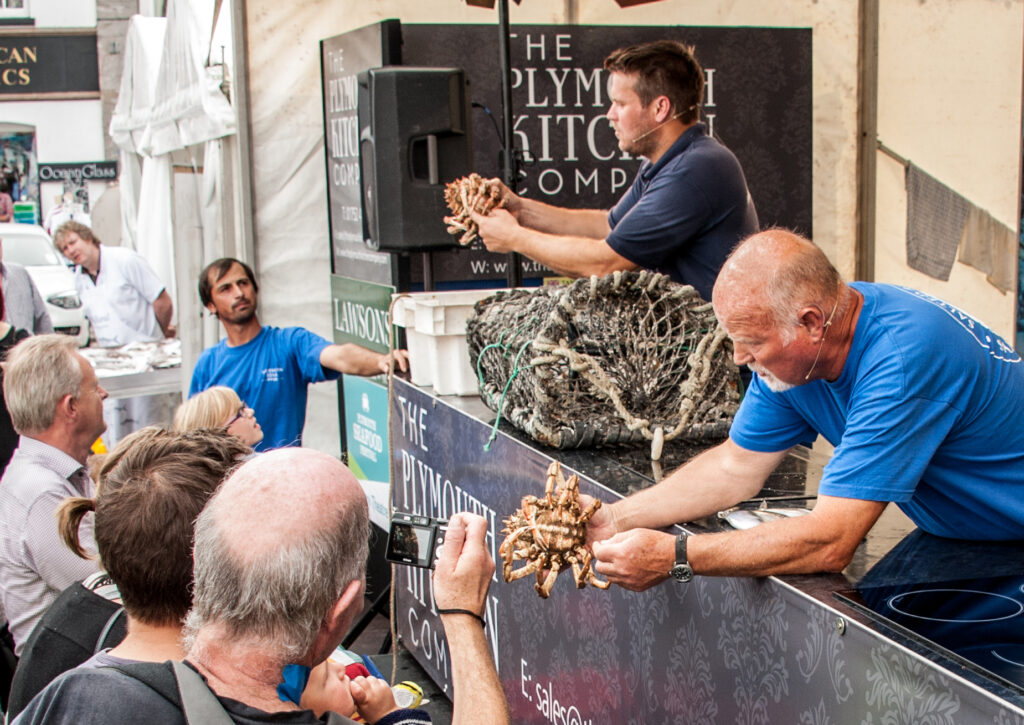 Two chefs conducting a live seafood demonstration hold out crabs to the crowd for a closer look.